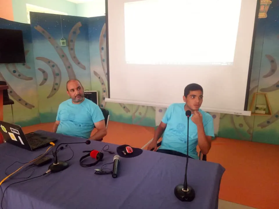 Coaching at a table in front of a projector screen at Community Challenge Day, Algiers, 2019.
